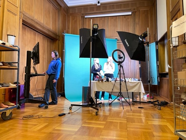 A professional photo studio featuring lighting equipment, a blue backdrop, and staff preparing for a photoshoot.