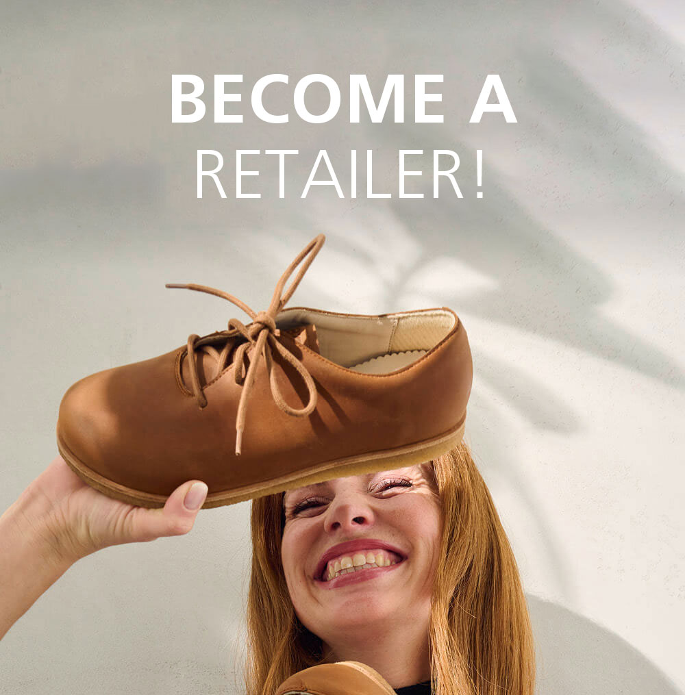 A smiling woman holds up a brown shoe with the text 'Become a Retailer!' in the background, encouraging participation in the shoe retail industry.