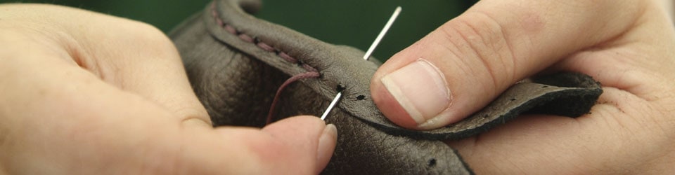 Close-up of hands carefully sewing a piece of leather with a needle
