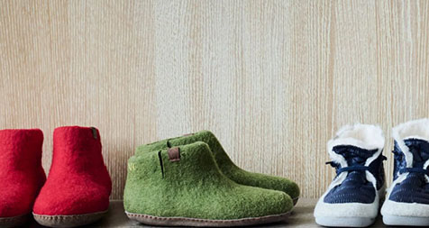 A row of three pairs of wool slippers in red, green, and blue colors displayed against a wooden background