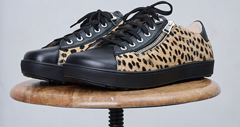 A pair of trendy sneakers featuring a leopard print design and black details, displayed on a wooden stool.