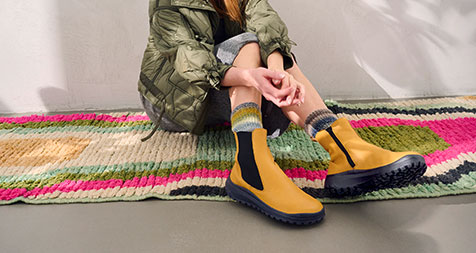 Person wearing yellow boots and colorful socks, sitting on a colorful rug