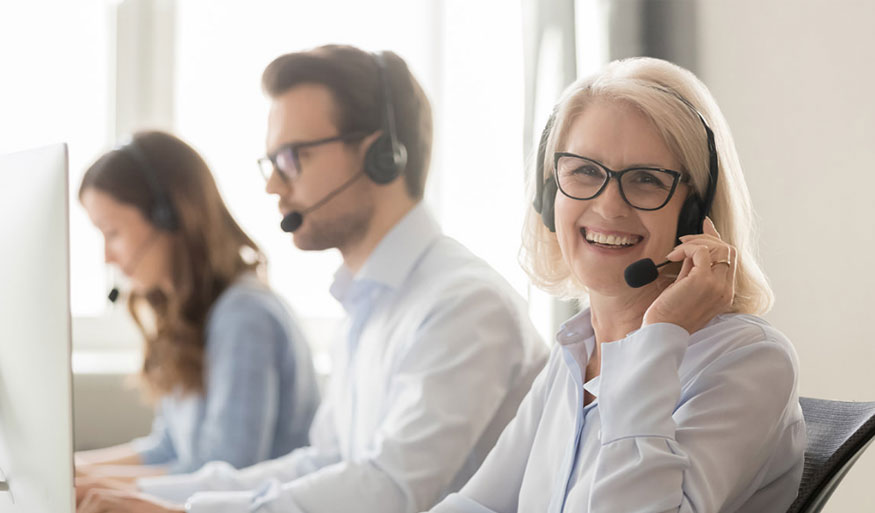 Three customer service representatives wearing headsets, smiling and assisting customers in a call center environment