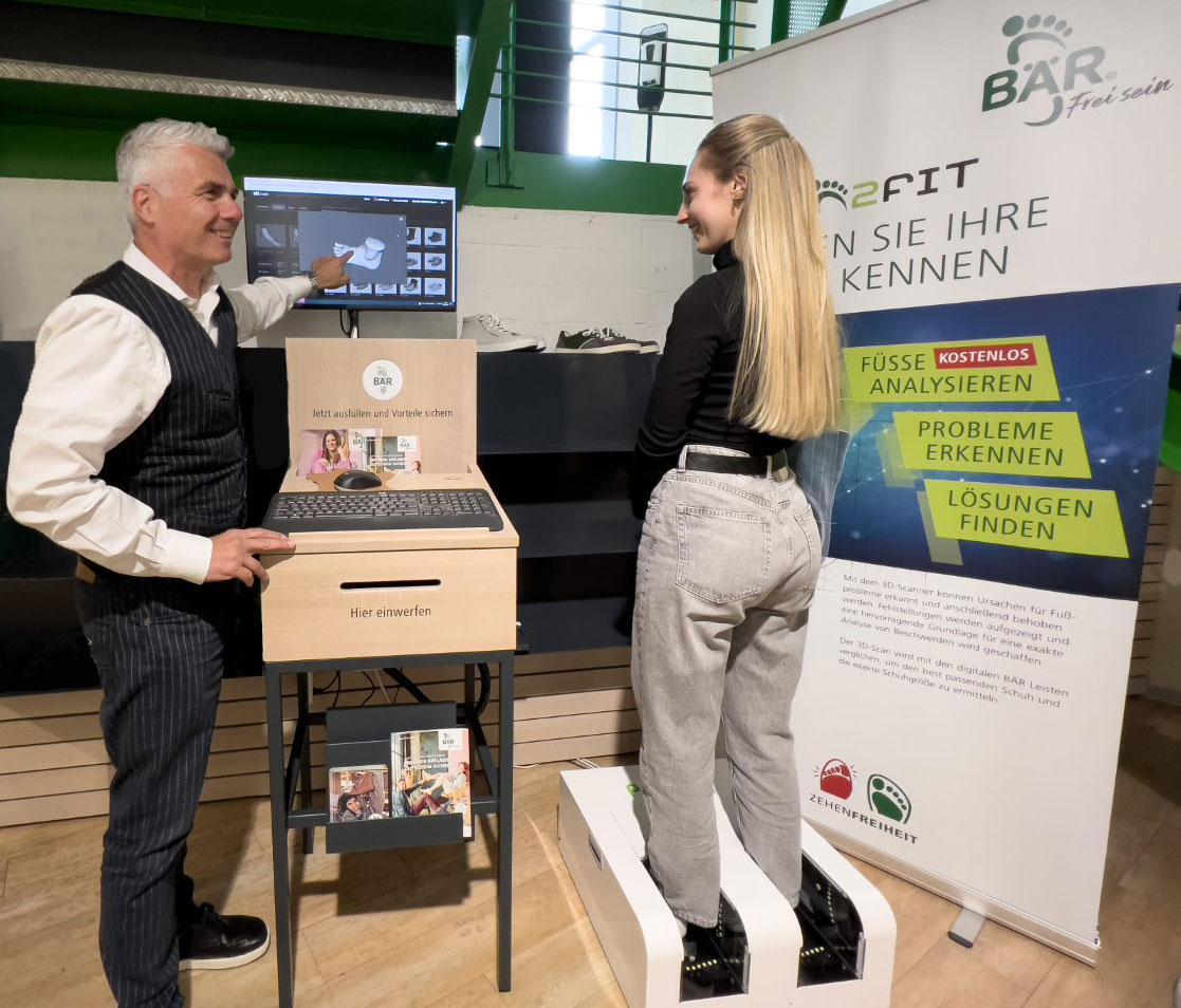 A man demonstrating foot analysis technology to a woman standing on a scanning device in a store.