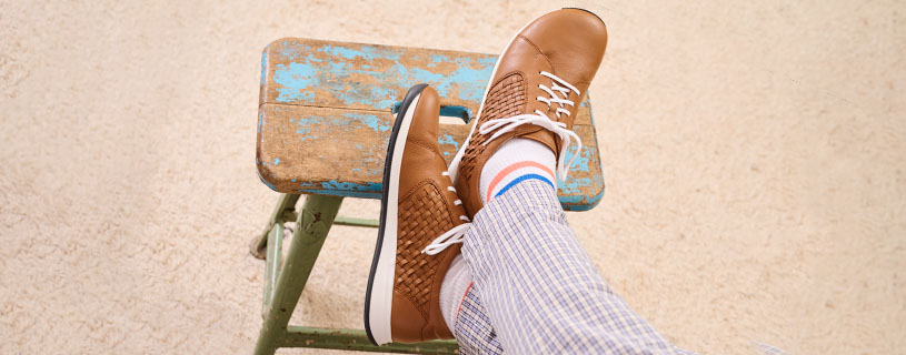Person wearing brown leather shoes with white laces, seated on a worn blue-green stool