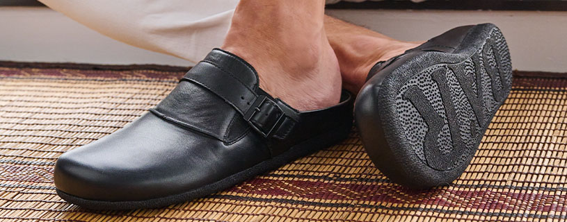 Person wearing black leather slip-on mules with buckle on woven mat