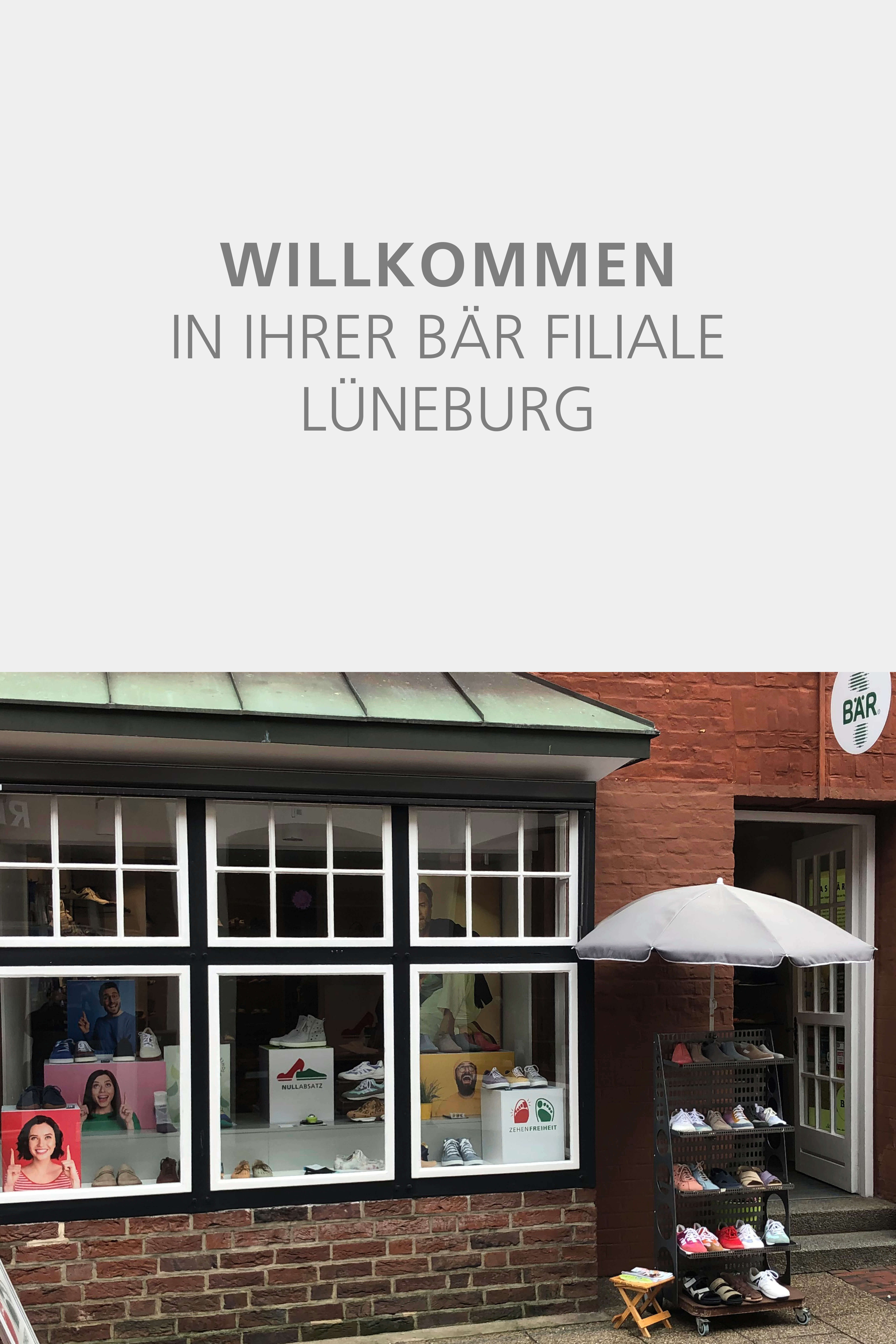 Exterior view of the BÄR store in Lüneburg with a welcoming sign and a display of shoes under an umbrella.