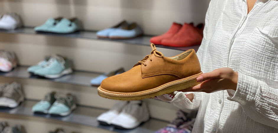 Person holding a brown leather shoe in a shop with various shoes displayed on shelves