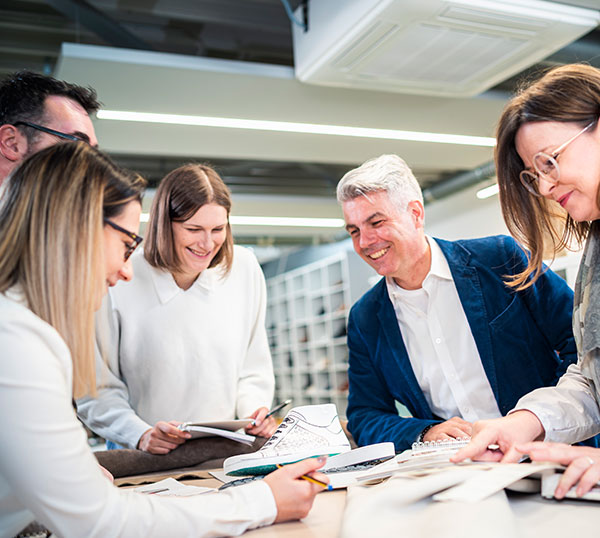 Group of professionals collaborating at a table in a modern office, surrounded by documents and designs.