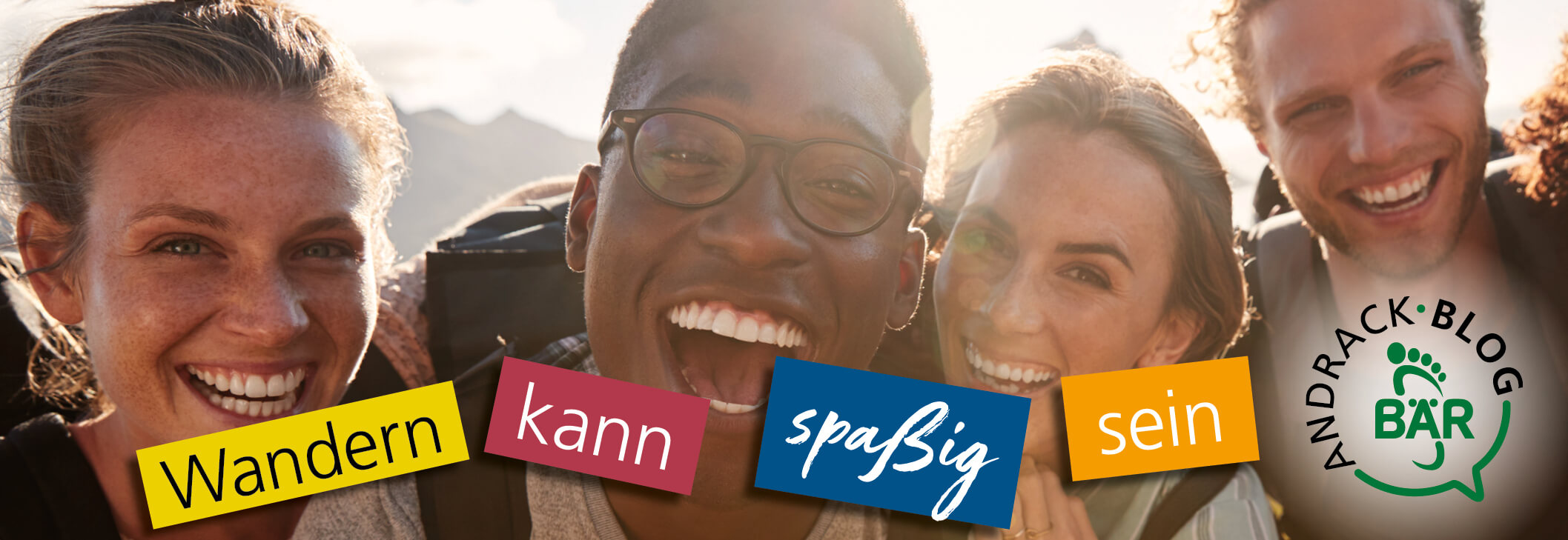 Four smiling friends enjoying a hiking trip with mountains in the background, promoting the Andrack Blog Bär and the idea that hiking can be fun.