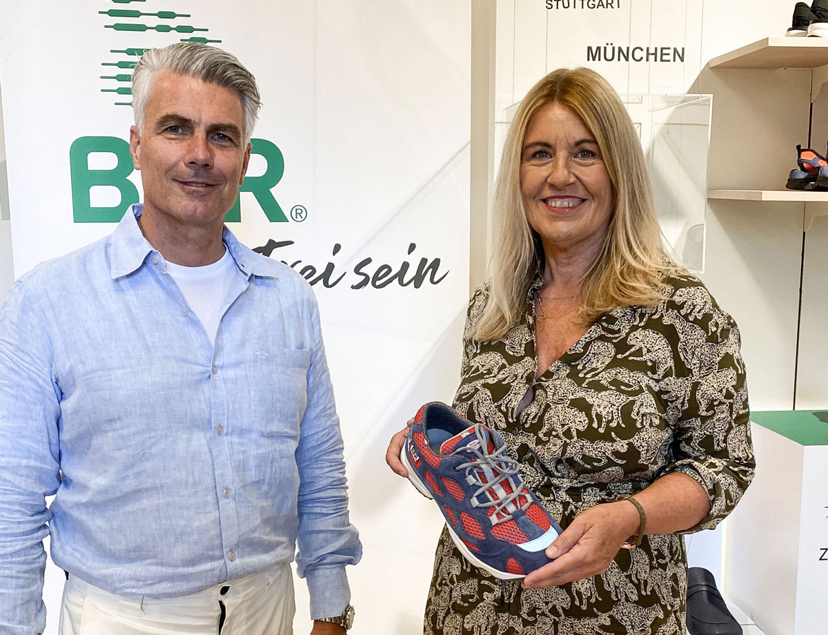 Two people at a business event presenting a red and blue sneaker