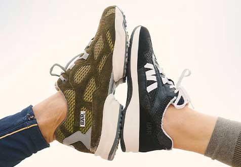 Two feet wearing stylish sneakers, one in olive green and the other in black with white accents, facing each other.
